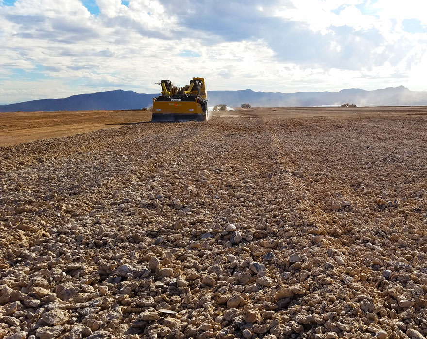 A Vermeer surface miner grinds rocks in front of a small mountain range