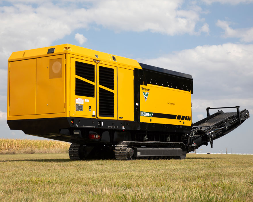 A large yellow slow speed shredder sitting next to a corn field