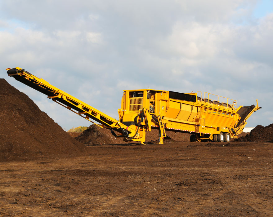 A trommel screen works next to a pile of organic matter