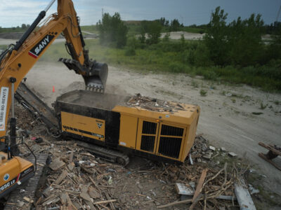 A machine drops wood waste into a Vermeer low speed shredder at a waste site