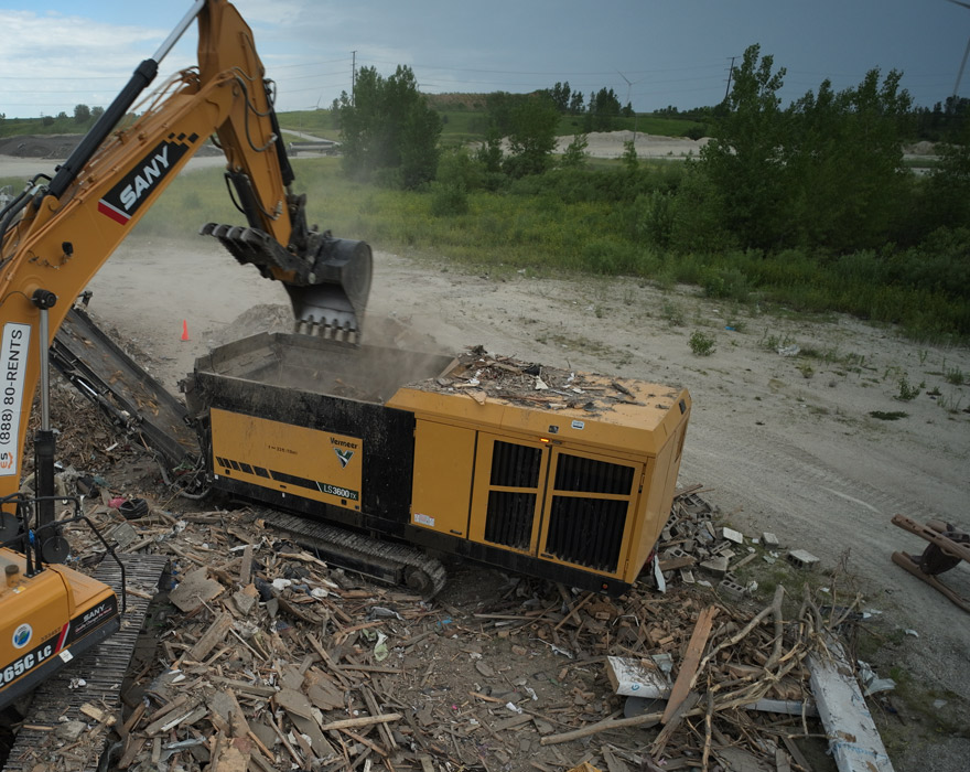 A machine drops wood waste into a Vermeer low speed shredder at a waste site