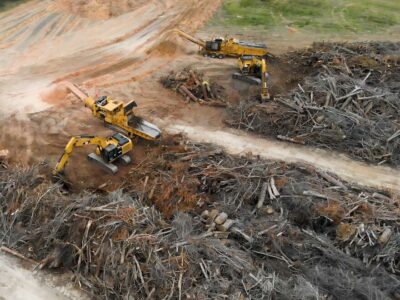 Aerial image of multiple large machines cleaning up extensive piles of downed trees