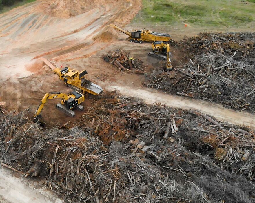 Aerial image of multiple large machines cleaning up extensive piles of downed trees