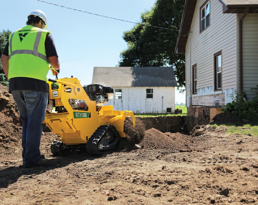 A man pushes a walk-behind trencher next to a house