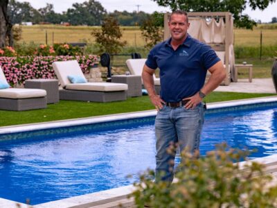 A man in a polo and jeans stands in front of a well manicured pool