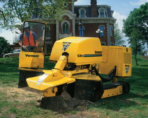 A man operates a Vermeer SC50TX stump grinder in front of a historical building