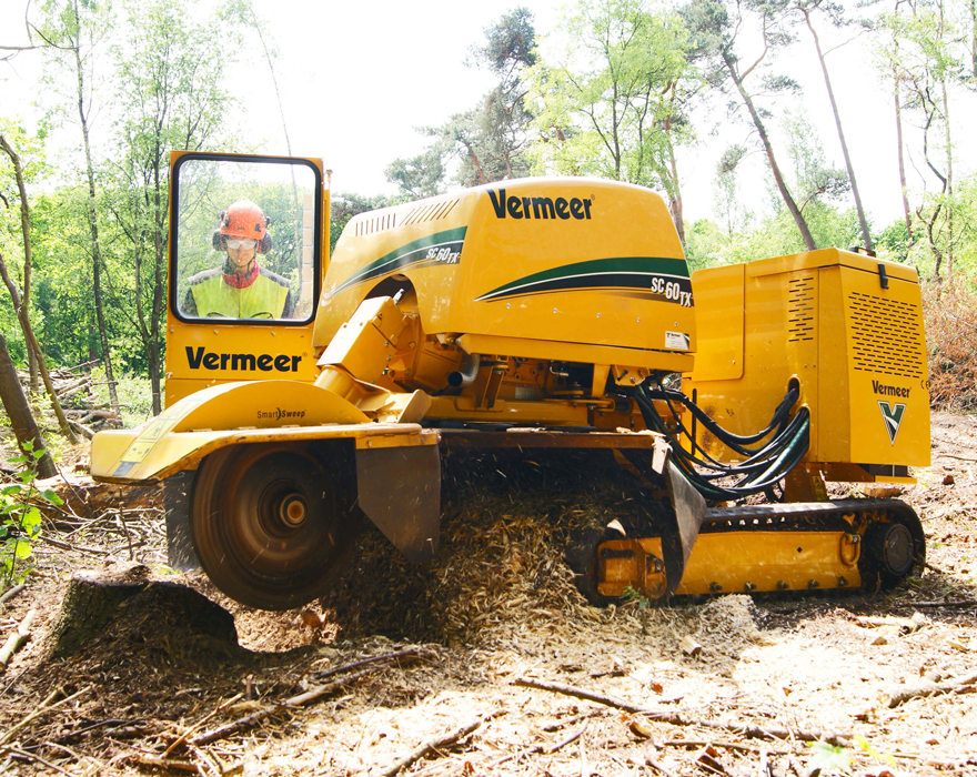 A man operates a SC60TX stump remover in a forest from behind a protective barrier