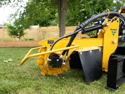 A Vermeer stump cutter attachment on a mini skid steer in a residential yard