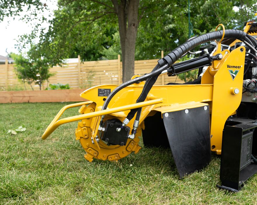 A Vermeer stump cutter attachment on a mini skid steer in a residential yard