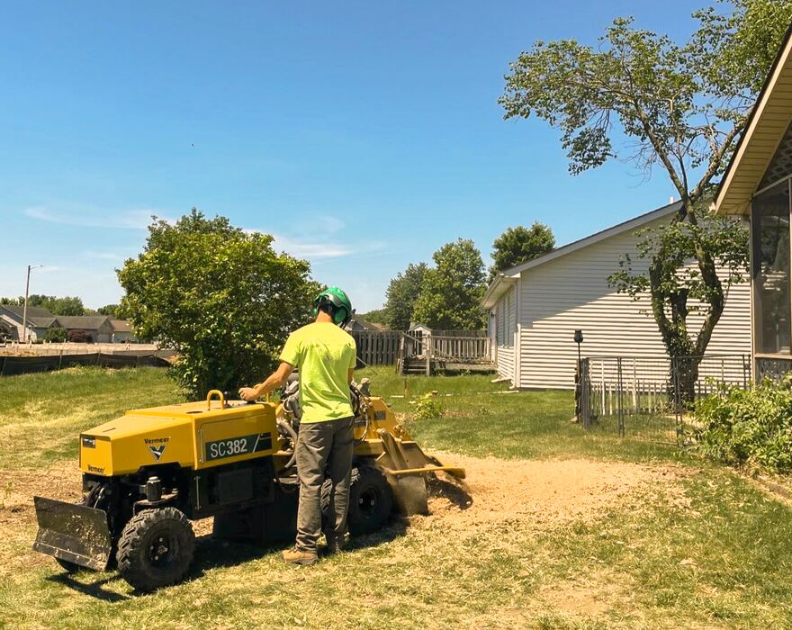 A man operates a stump cutter in a residential backyard