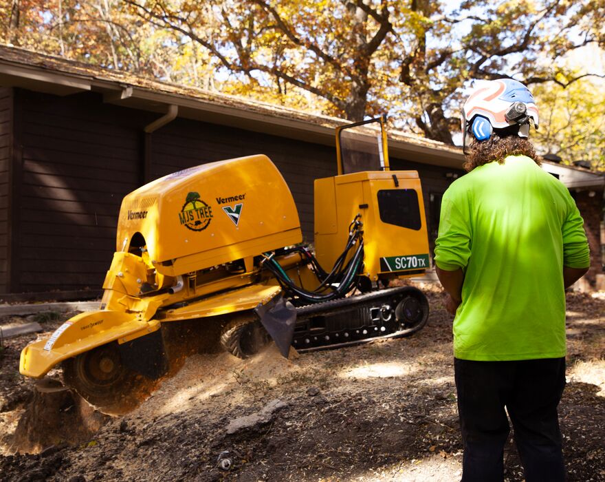 A man stands next to a stump cutter, operating it. 