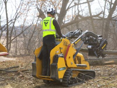 A person operating a mini skid steer with a log grapple attachment