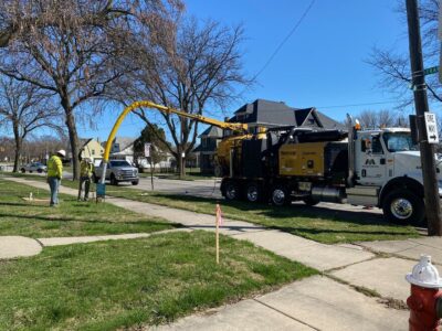 Two individuals stand by a road using a Vermeer vacuum truck for utility work.