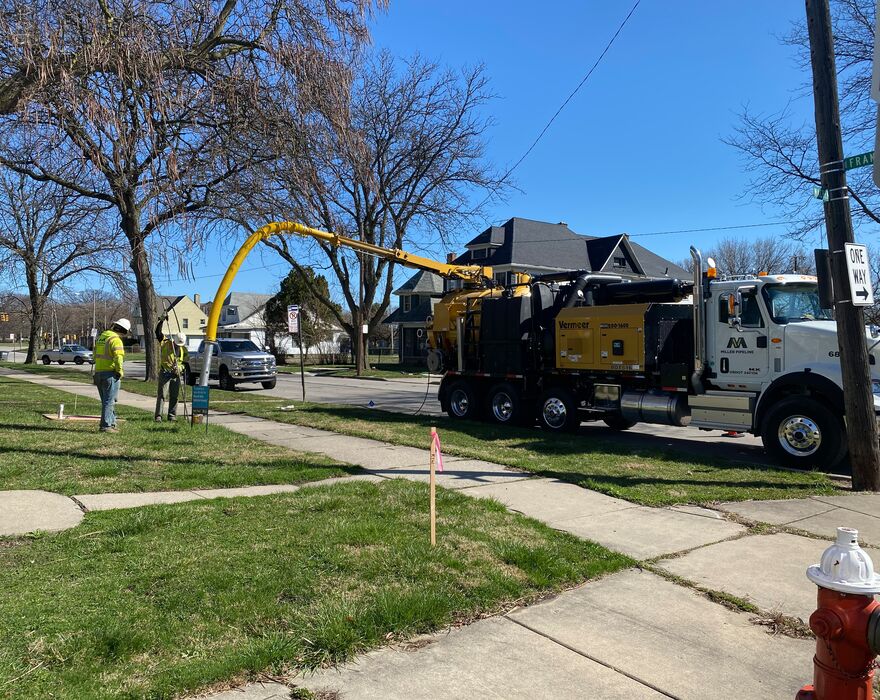 Two individuals stand by a road using a Vermeer vacuum truck for utility work.