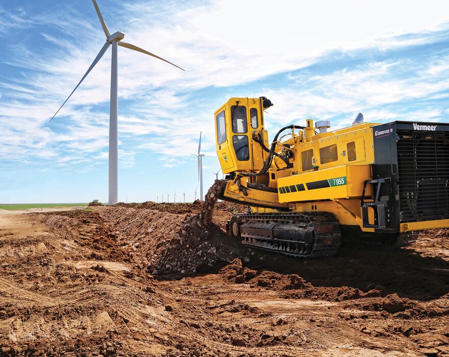 A large trencher trenching in a field near a wind turbine