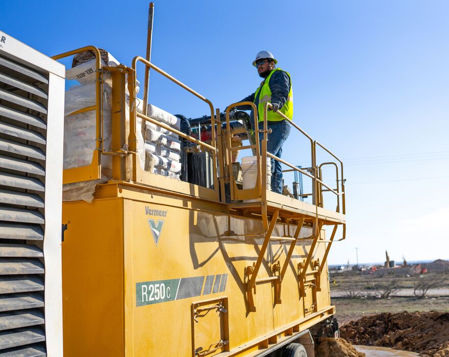 A man stands on the top of a R250c reclaimer in a pipeline field