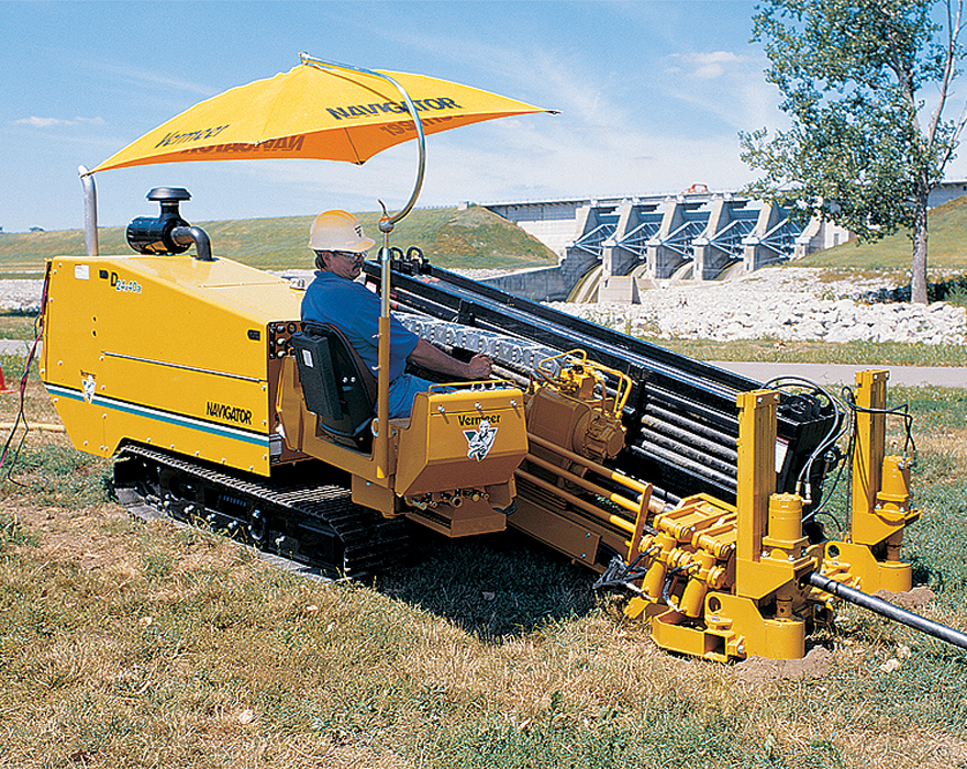 A man sits on a horizontal directional drill that is working in front of a dam