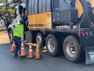 A man stands next to a vacuum excavation truck and moves traffic cones