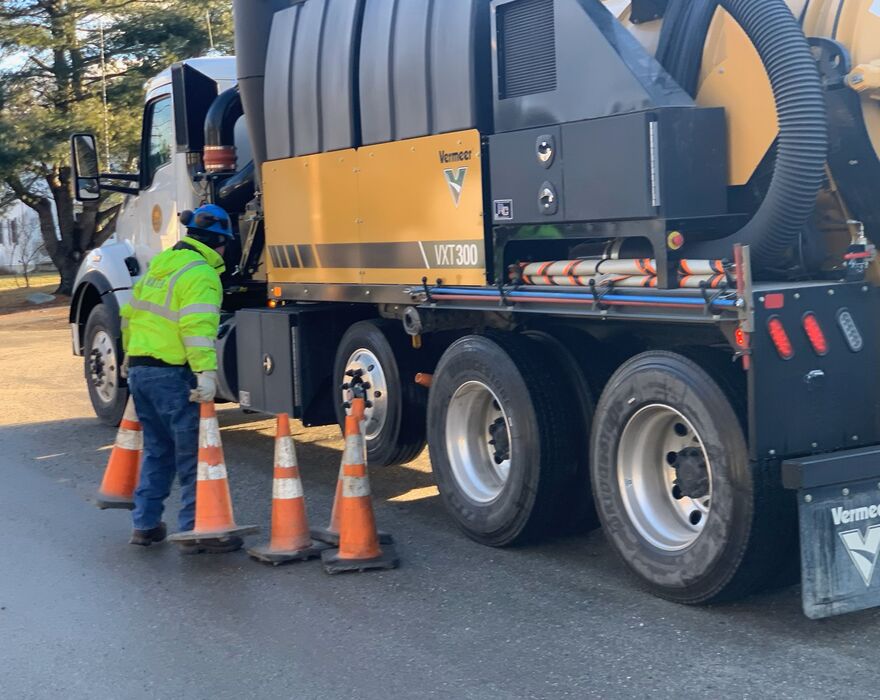 A man stands next to a vacuum excavation truck and moves traffic cones