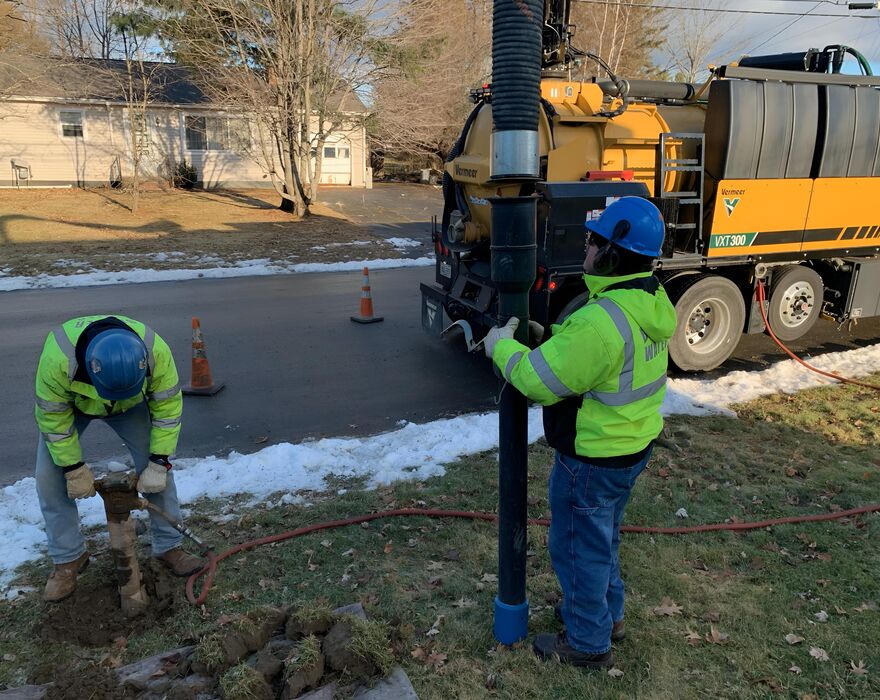 Two men work next to a road with a vacuum excavation truck