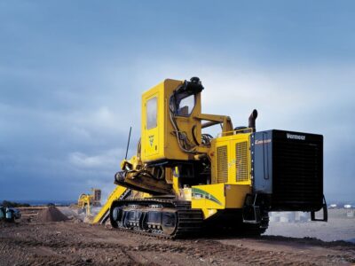 A yellow Vermeer pipeline trencher on a jobsite in front a dark sky.