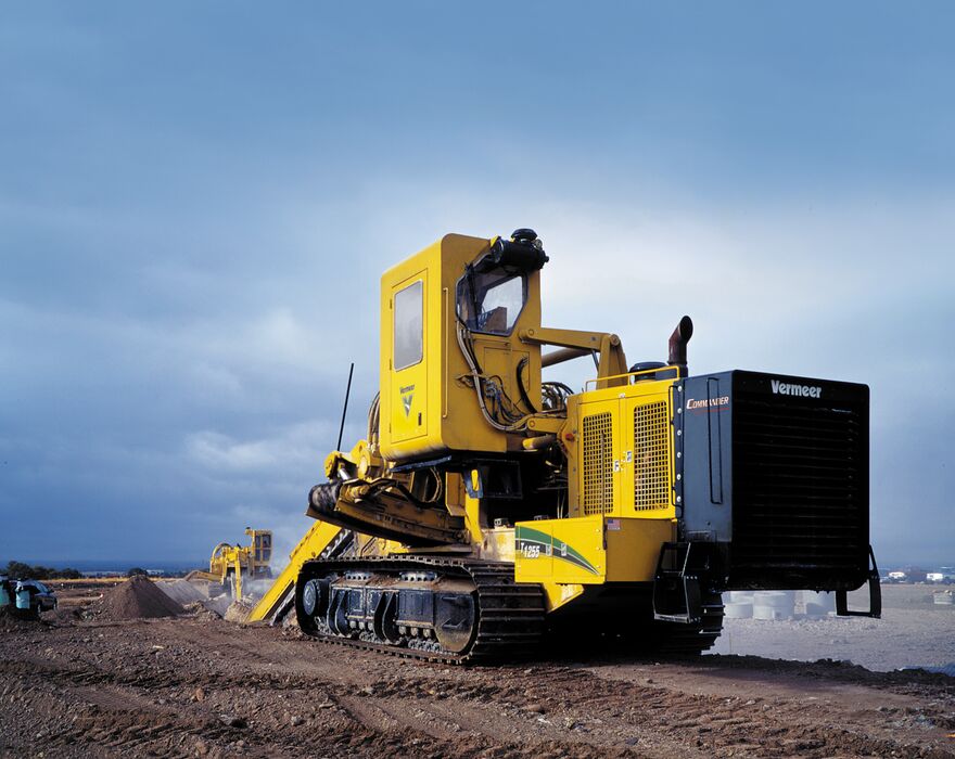 A yellow Vermeer pipeline trencher on a jobsite in front a dark sky.