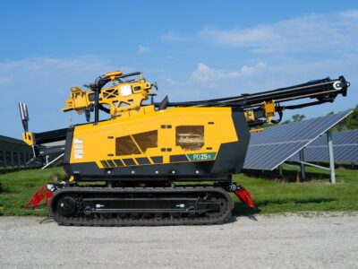 A pile driver sits in a solar field with a folded mast