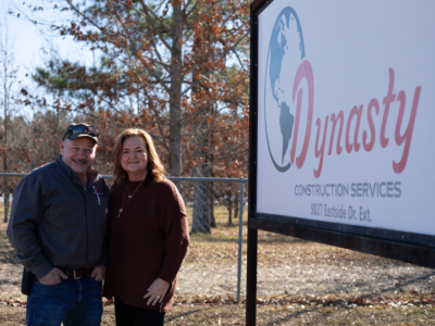 Owners of Dynasty Construction Services stand next to their business sign