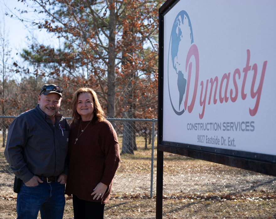 Owners of Dynasty Construction Services stand next to their business sign